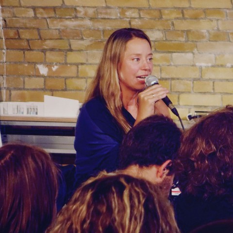 Uta Mühleis long blonde hair on stage with a microphone