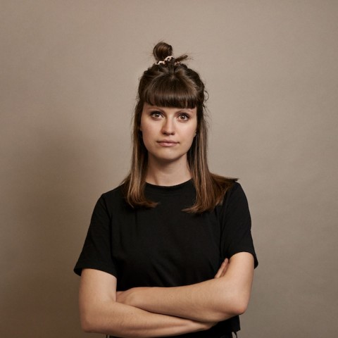 Linda Dudacy long  brown hair dressed in black in front of grey background crossing her arms
