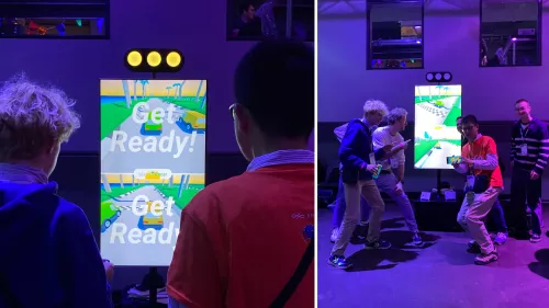Links: Zwei Spieler stehen vor dem Window Arcade und machen sich für das Autorennen bereit. Rechts: Ein Gruppe von Spieler*innen vor der Window Arcade Station.