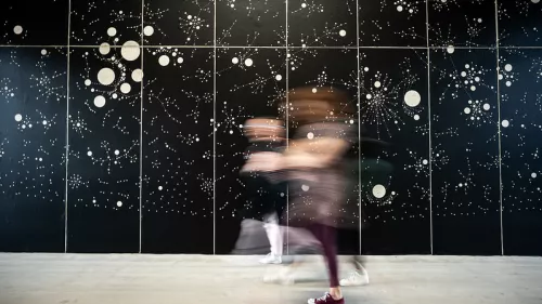 Kunstinstallation – viele helle Punkte auf einer Wand, davor Menschen
