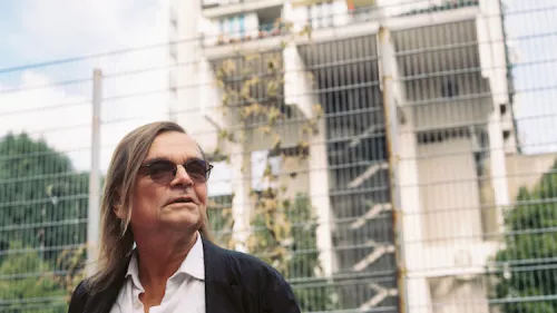 Das Foto zeigt ein Portrait von Diedrich Diederichsen. Er trägt Brille, schulterlanges glattes Haar und schaut seitlich in die Kamera. 