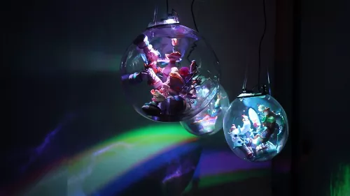 Three bubbles hang suspended in a dark scenery. Each bubble contains a colourful, miniature world. Colourful, rainbow light refractions are cast onto the wall.