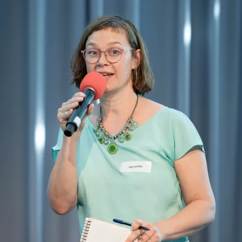 Inga Schiffler spricht in ein rotes Mikro. In der Hand hält sie einen Block und einen Stift.
