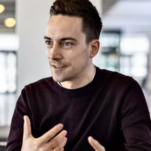 Lukas Brand, weinroter Pullover, in einer Kaffeeteria, im Gespräch 