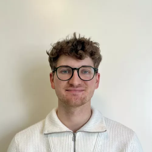 Foto von Keno Brieger; lächelnd, mit Brille und weißem Oberteil