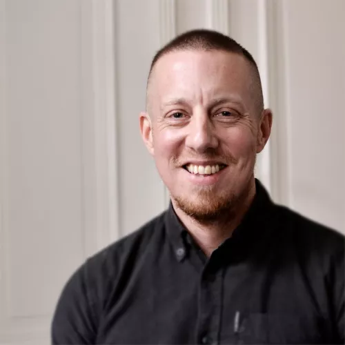 Florian Köhler lächelnd im Portrait mit schwarzem Hemd vor hellem Hintergrund