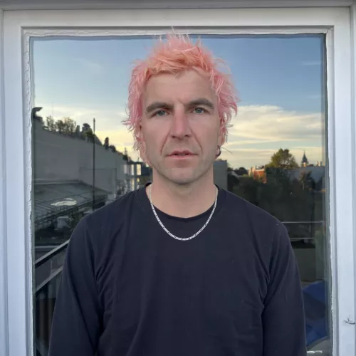 Mika Amsterdam Pressefoto. Pinke Haare. Auf einem Balkon.