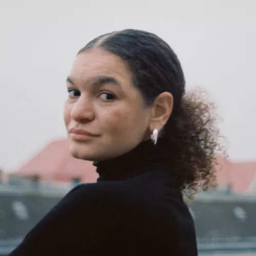 Portrait von Noëmi Sander, Blick über die Schulter vor nebeligen Häuserdächern im Hintergrund 