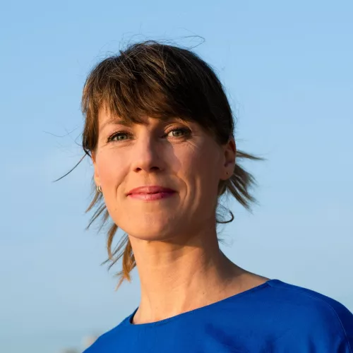 Eine Frau mit mittelblonden Haaren und seitlichem Pony lächelt selbstbewusst in die Kamera. Sie trägt ein marineblaues Shirt.