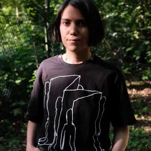 frontal image of Ipek Burçak, a light-brown skinned female person standing in the nature wearing a black T-shirt, short brown hair, showing her upper body