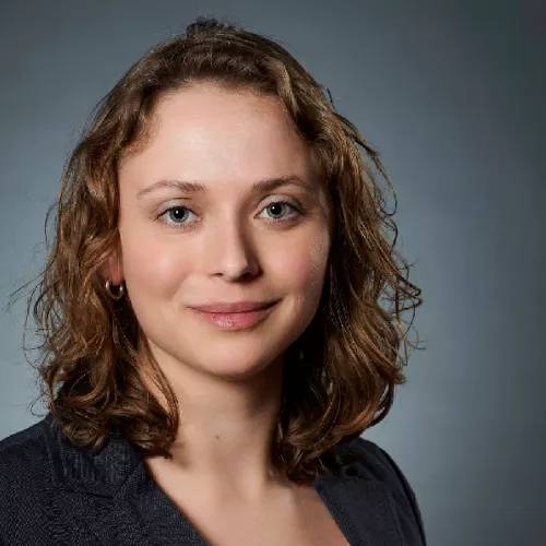Eine Frau mit lockigen Haaren, die freundlich in die Kamera schaut.