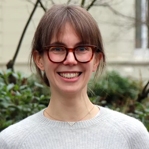 Antonia Eichenauer lächelt in die Kamera. Sie hat einen Pony, eine große Brille und trägt einen grauen Pulli.