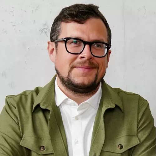 Thomas Lückerath mit schwarzer Brille und grünem Sakko.