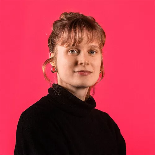 Portrait einer blonden Frau mit schwarzem Rollkragenpulli vor rotem Hintergrund