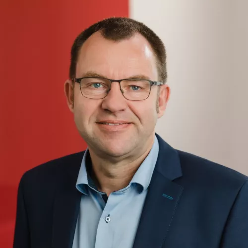 Zu sehen ist ein Portrait von Frank Ziegele. Er hat braune Haare, trägt eine Brille sowie ein hellblaues Hemd und ein dunkelblaues Jackett.