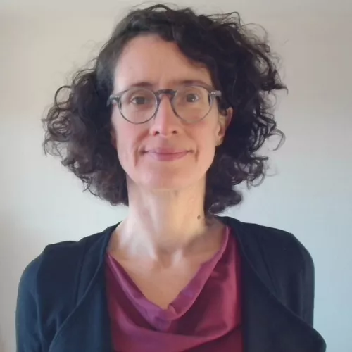 Jana Mattert hat ein schmales Gesicht, dunkles krauses Harr und trägt Brille.