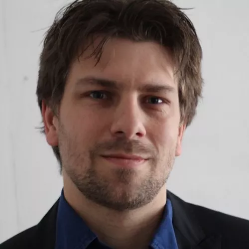 Photo of Julien Colomb, caucasian man with short dark-blond hair and a 3-days bard. He wears a jacket and a blue shirt. Note the photo is about 10 years old.