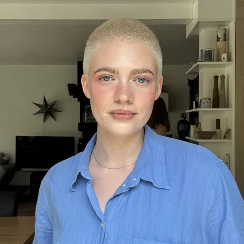 Auf dem Foto blickt Amira Blätter direkt in die Kamera. Amira trägt ein blaues Hemd und hat kurze blonde Haare.